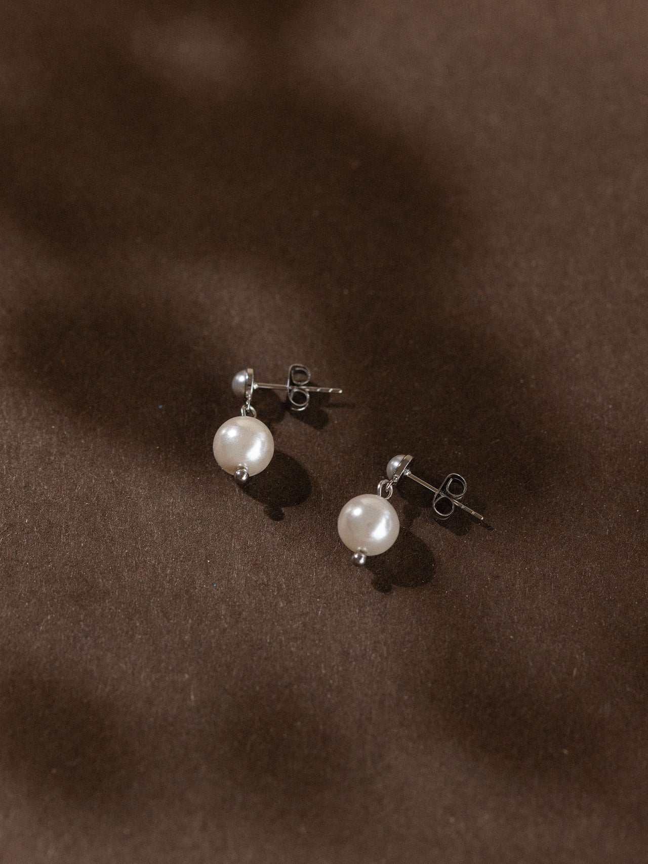 Elegante, allergenfreundliche Ohrringe mit weißen Perlen von PURELEI auf dunklem Hintergrund.