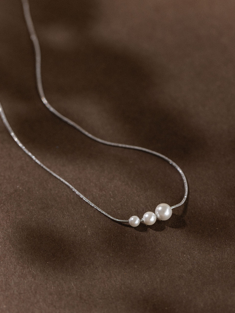 Zarte PURELEI Kette mit drei matten, runden Anhängern auf dunklem Hintergrund.