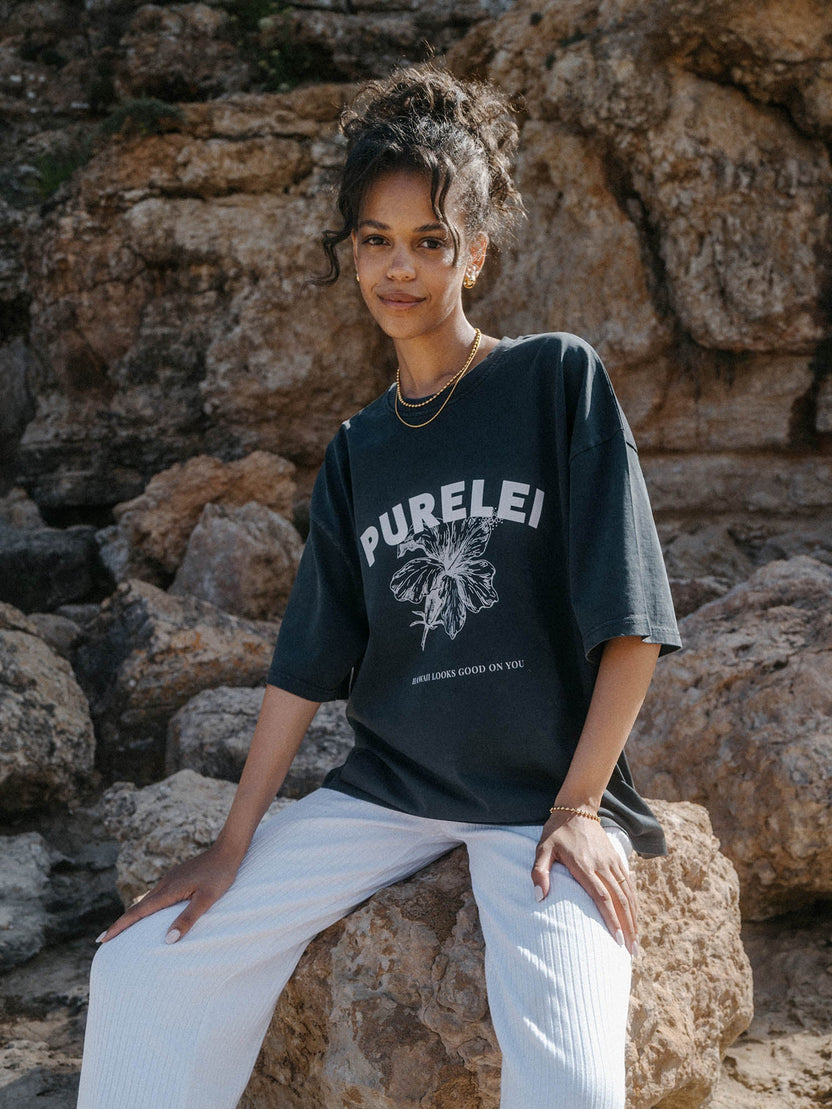 Schwarzes T-Shirt mit PURELEI-Print, lässig getragen vor Felsen, entspannte Stimmung.