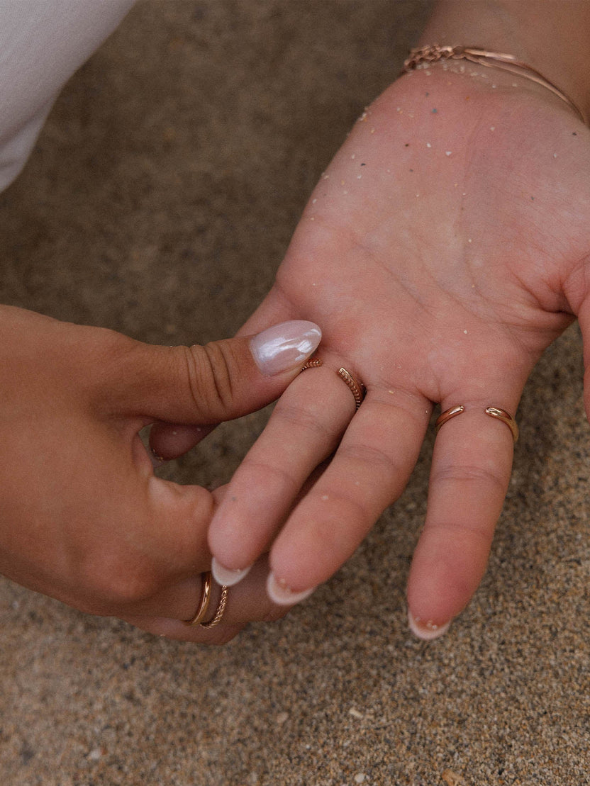 Roségoldene Ringe auf einer Hand, umgeben von Sand – PURELEI Eleganz und Natürlichkeit.