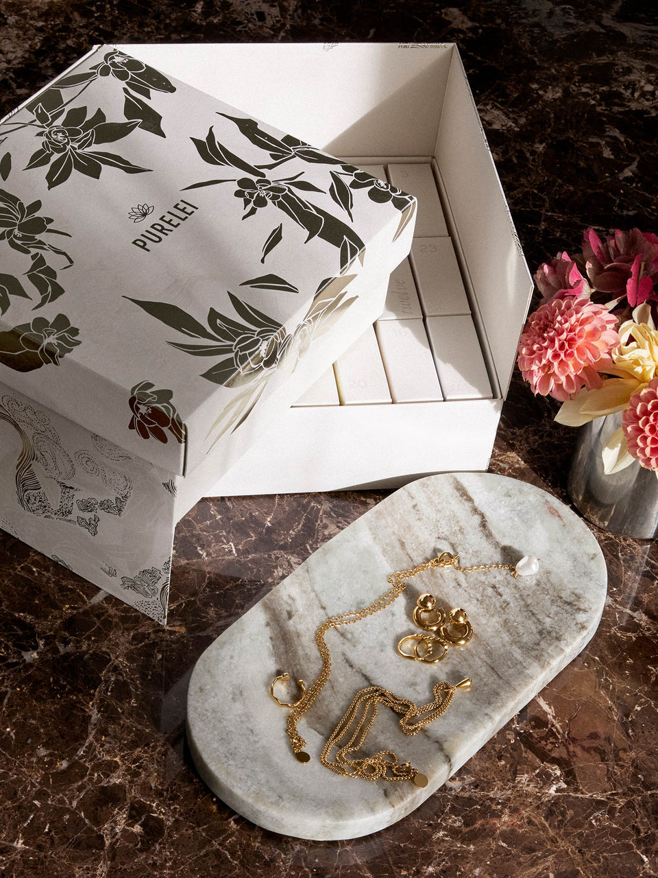 Elegante PURELEI Schmuckstücke auf marmoriertem Untergrund, umgeben von natürlicher Schönheit.