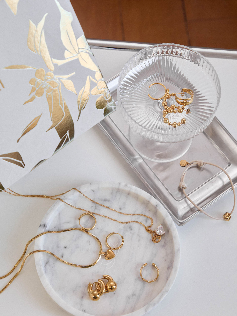 Goldene Schmuckstücke von PURELEI auf marmoriertem Teller, elegant und feminin.