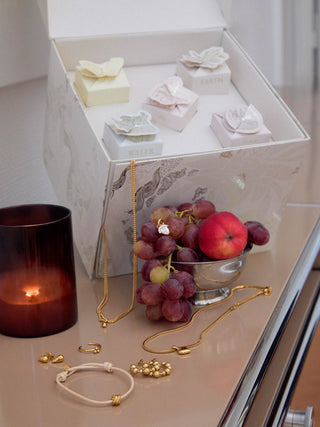 Elegante PURELEI Schmuckstücke in Roségold und Weiß, umgeben von frischen Früchten und Kerzenlicht.