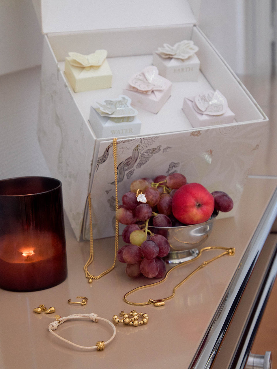 Elegante PURELEI Schmuckstücke in Roségold und Weiß, umgeben von frischen Früchten und Kerzenlicht.