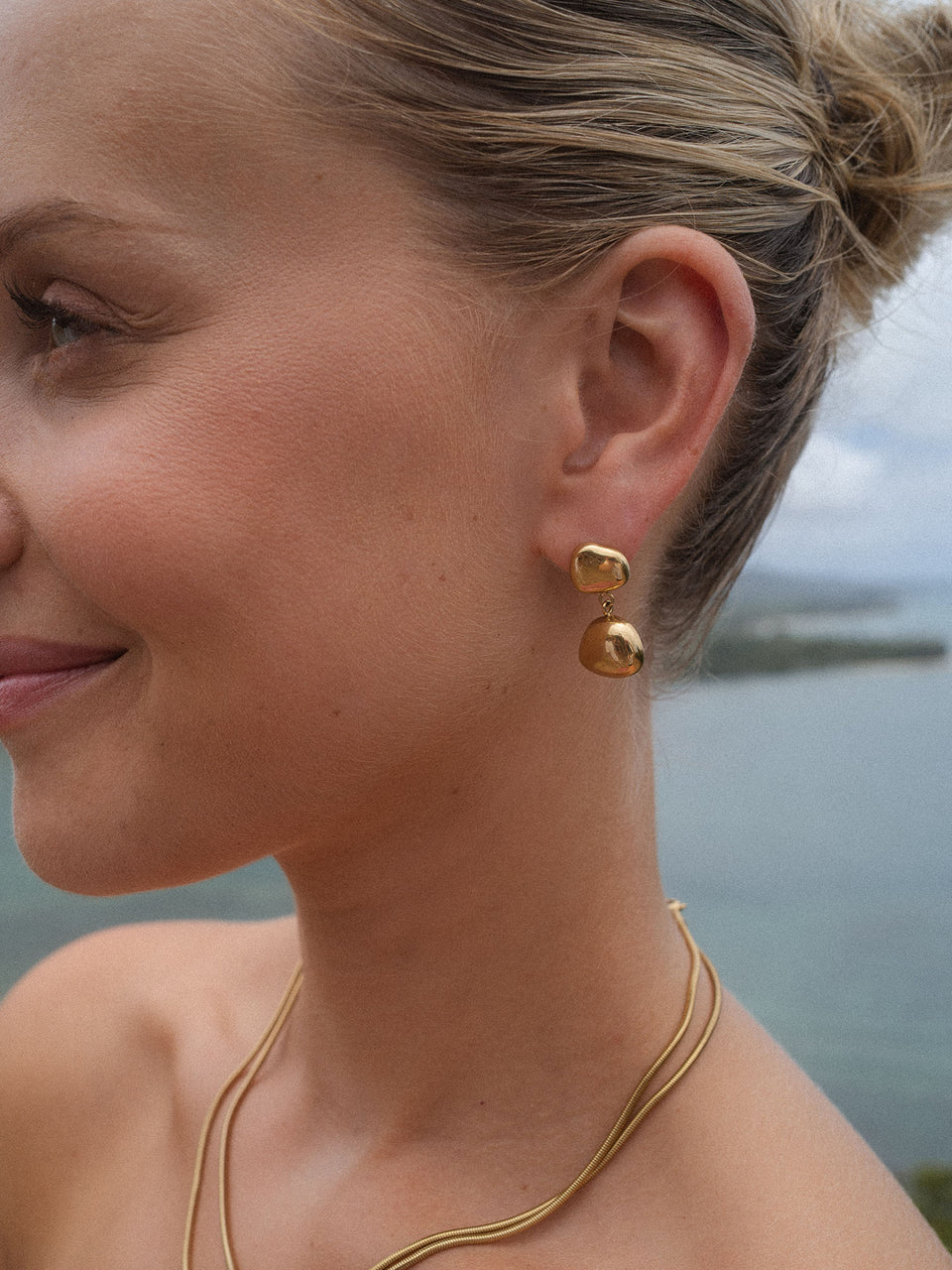 Roségoldene Ohrringe mit geschwungenem Design, getragen in maritimer Umgebung – PURELEI.