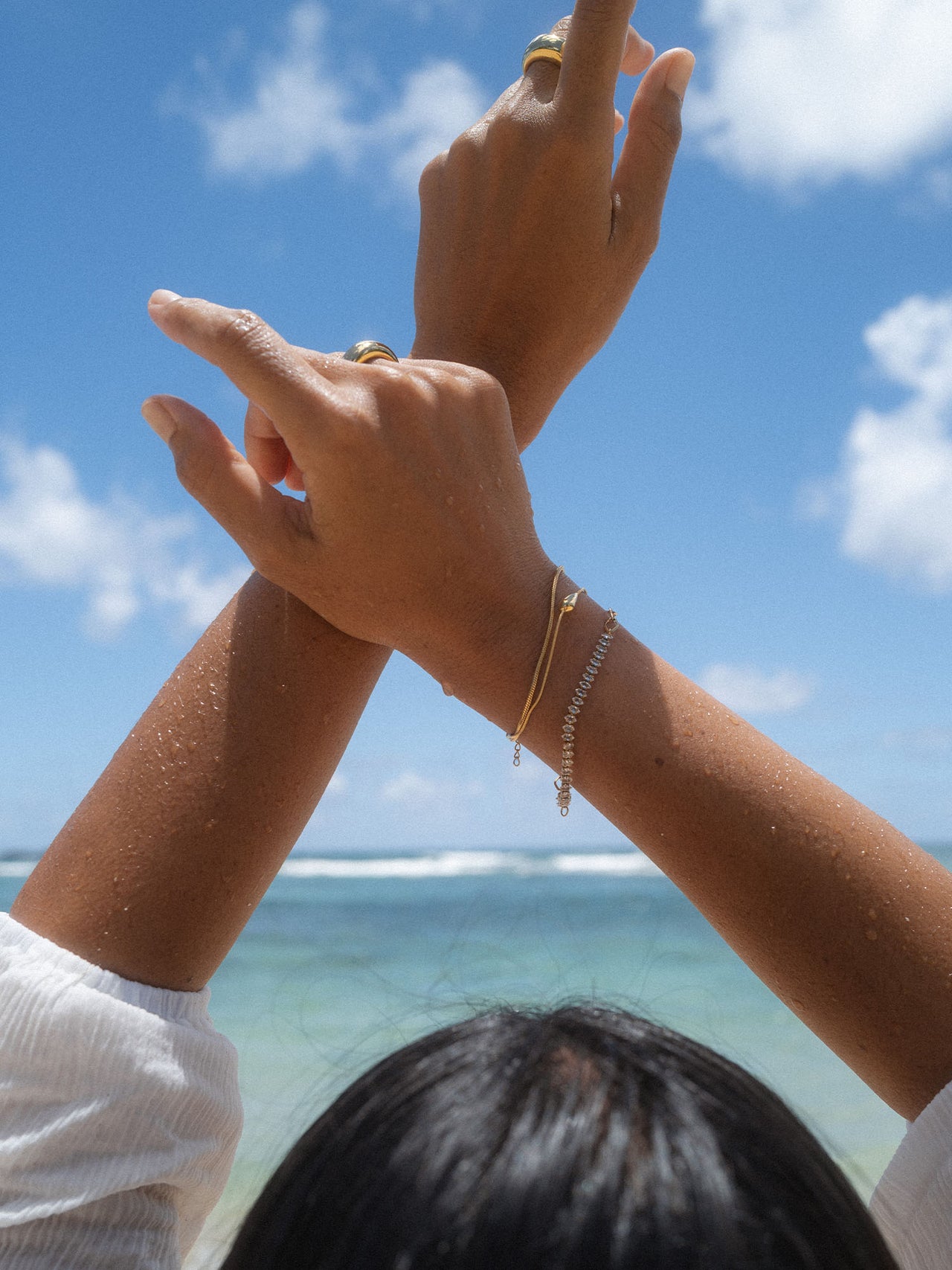 Zarte PURELEI Armbänder aus Silber, getragen am Strand unter blauem Himmel.