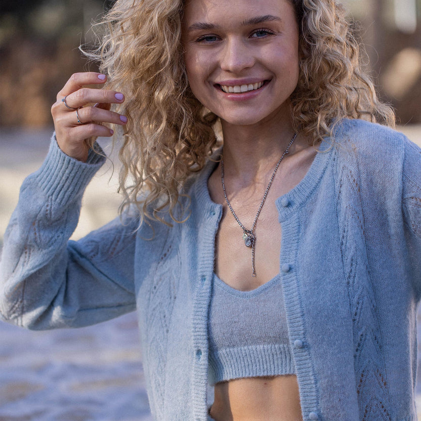 Zarte, silberne Kette mit Anhänger, getragen von lächelnder Frau in blauer Strickjacke – PURELEI.