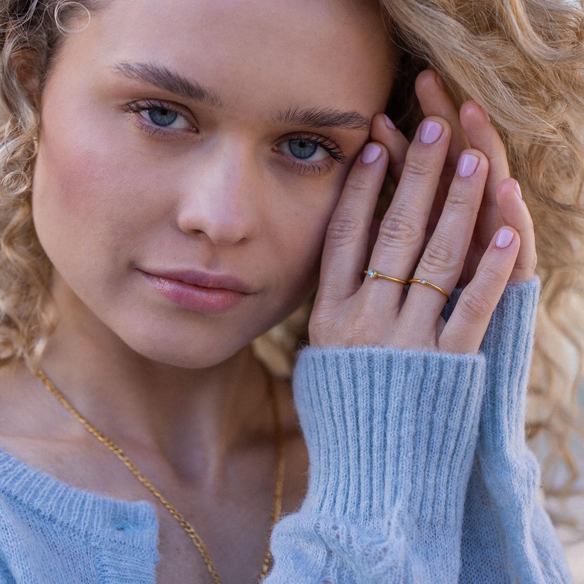 Zarte Ringe aus Gold mit funkelnden Details, getragen von einer Frau in einem blauen Pullover – PURELEI.