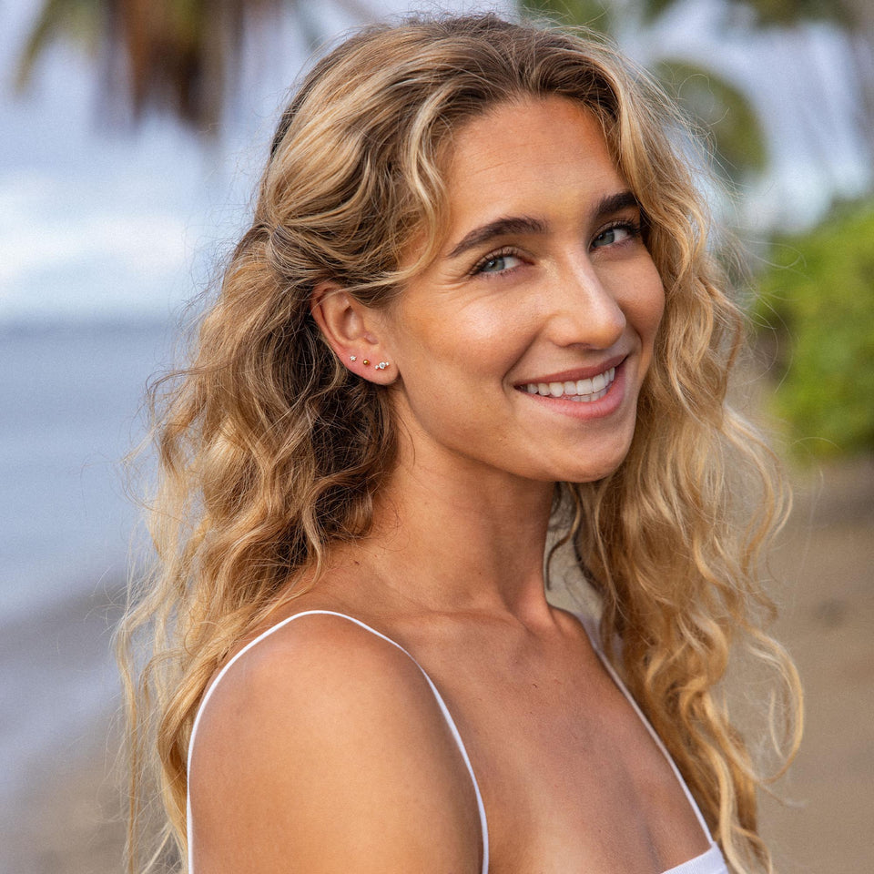 Feminine Ohrringe mit funkelnden Details, getragen von einer lächelnden Frau am Strand – PURELEI.