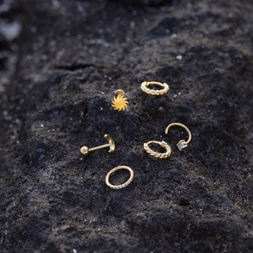 Goldene Ohrringe und Piercings auf dunklem Lavagestein, inspiriert von PURELEI.