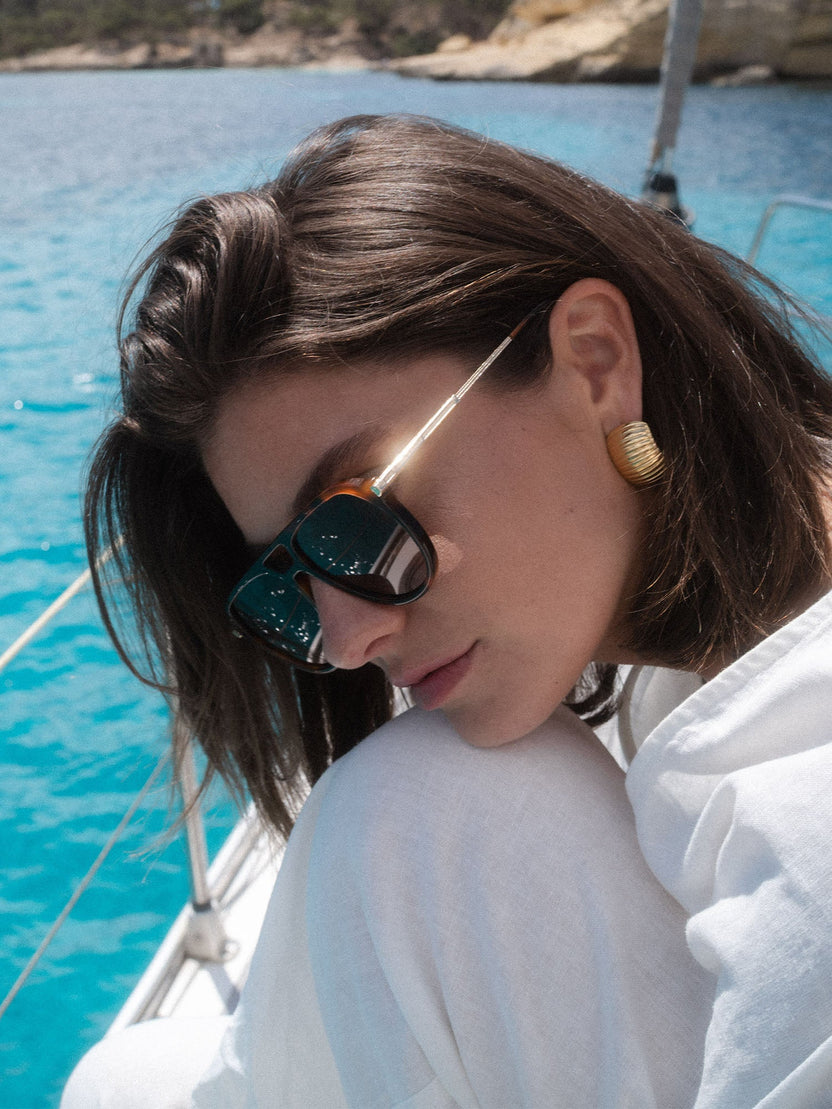 PURELEI Palm Beach Sonnenbrille im braunen Schildpatt-Look mit goldenem Bügel, elegant am Sommerstrand getragen.