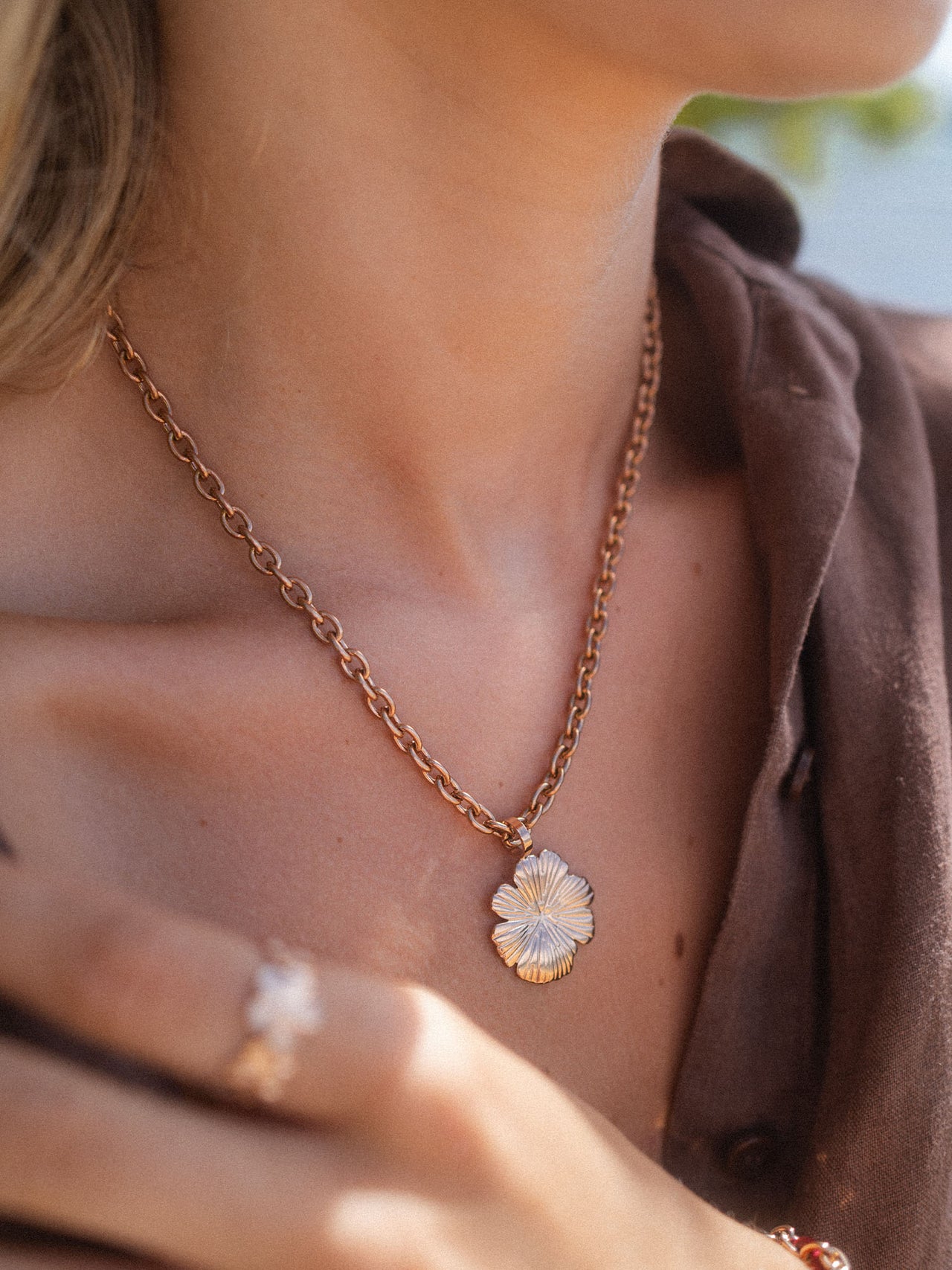Roségoldene Kette mit blütenförmigem Anhänger, getragen in warmem Licht – PURELEI.