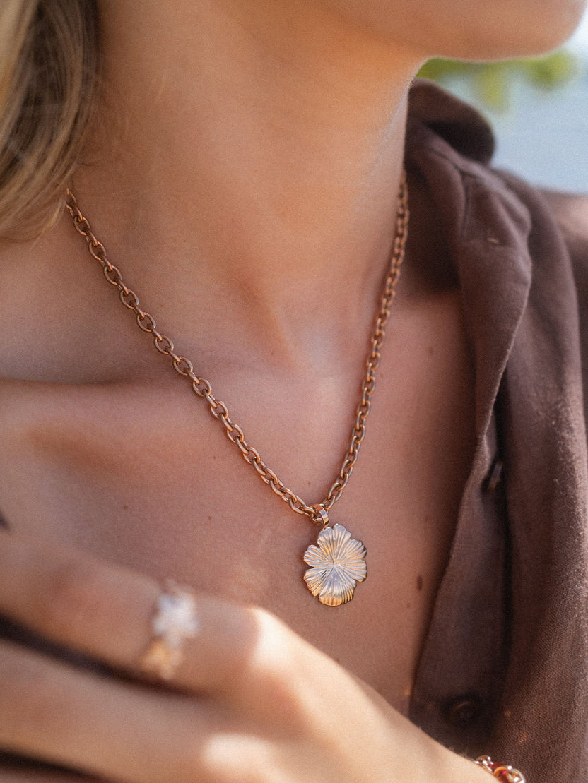 Roségoldene Kette mit blütenförmigem Anhänger, getragen in warmem Licht – PURELEI.