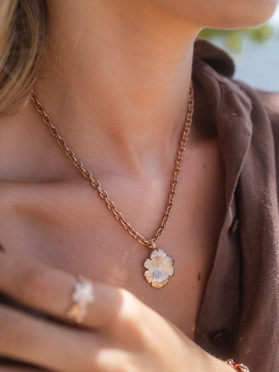 Roségoldene Kette mit blütenförmigem Anhänger, getragen in warmem Licht – PURELEI.