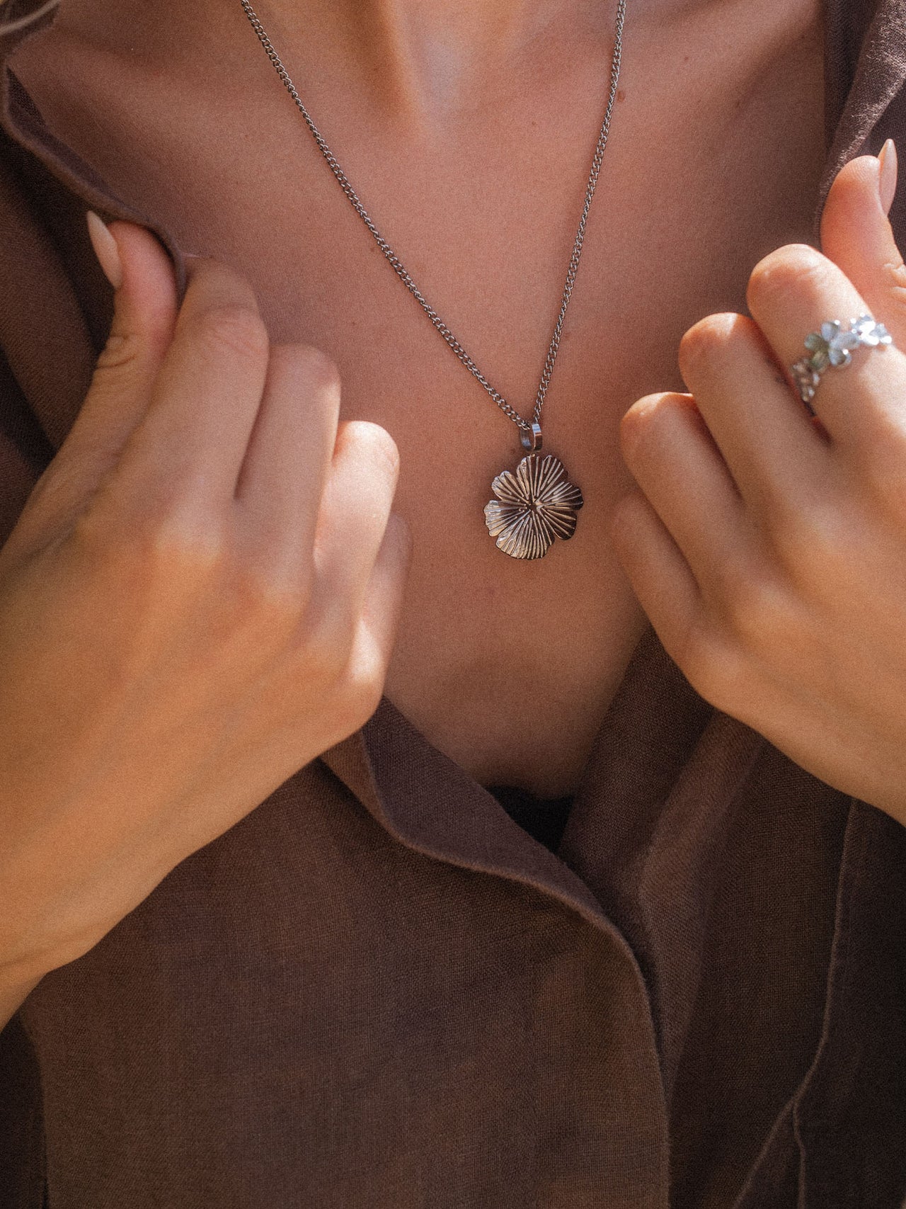Silberne Blütenkette von PURELEI, elegant und feminin, getragen auf braunem Stoff.