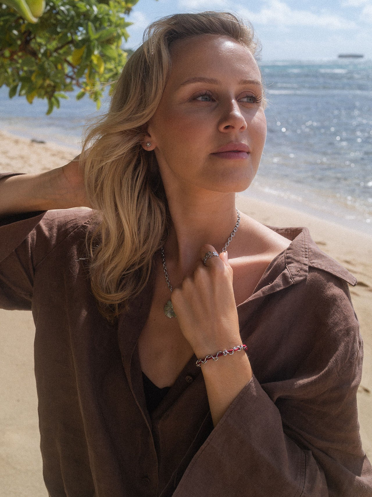 Silberne Kette und Armband von PURELEI, elegant am Strand getragen, mit Muschel-Detail.