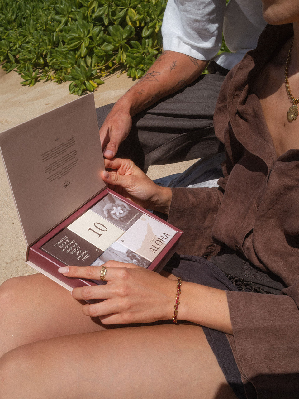 Händedetails mit PURELEI Ring und Armband, Aloha-Buch im Hintergrund, entspannte Stimmung.