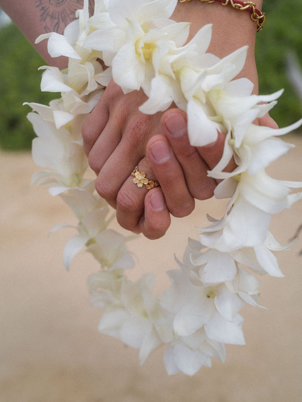 Hände mit zartem Ring und weißer Blumenleih, PURELEI inspiriert von tropischer Eleganz.