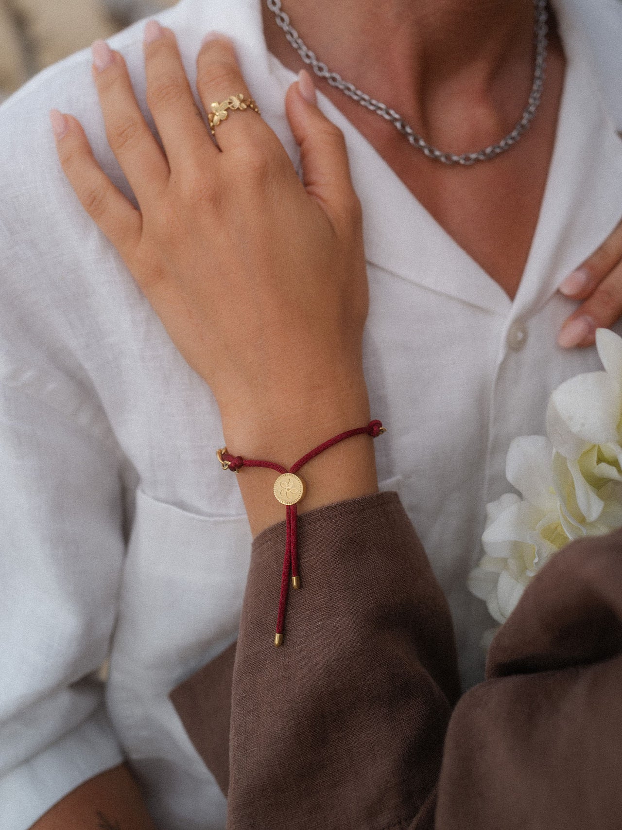 Braunes Armband mit goldfarbenem Anhänger, getragen mit elegantem Outfit, PURELEI.