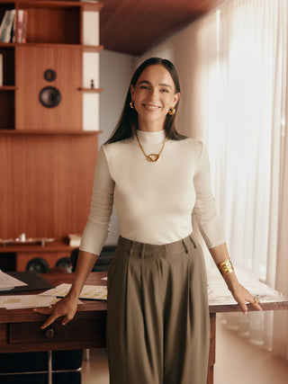 Elegante Frau mit PURELEI Schmuck, goldene Ohrringe und Kette, warmes Licht, stilvolles Ambiente.