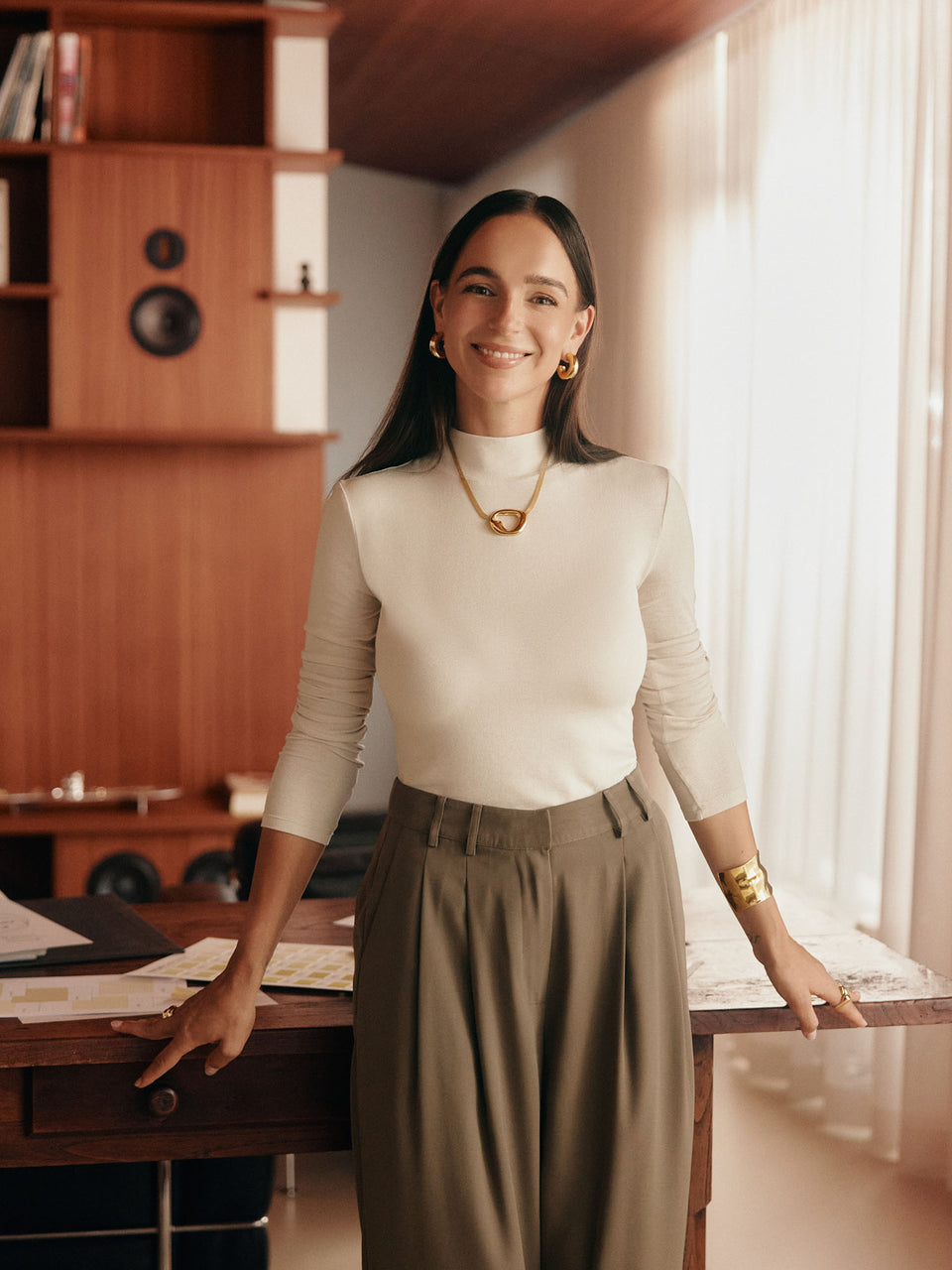 Elegante Frau mit PURELEI Schmuck, goldene Ohrringe und Kette, warmes Licht, stilvolles Ambiente.