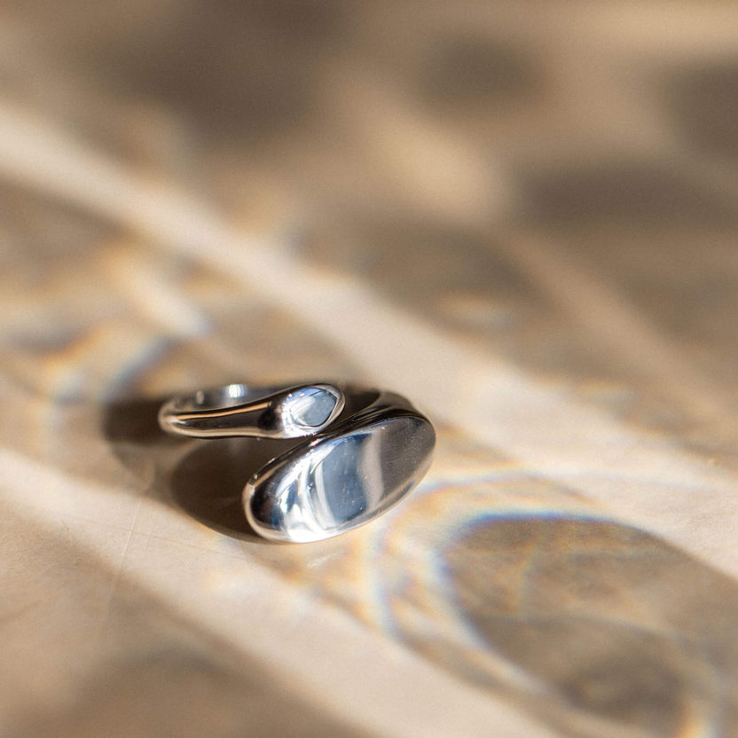 Silberner Ring mit geschwungenem Design auf sanftem Hintergrund, PURELEI inspiriert.