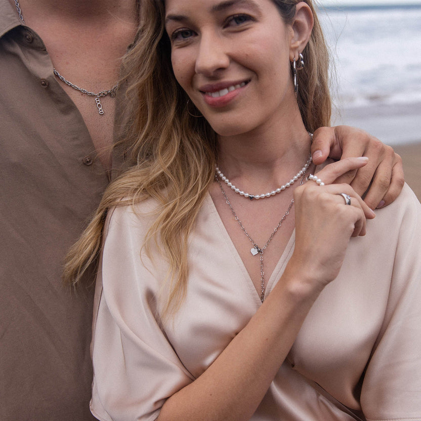 Elegante PURELEI Ketten aus Silber und Perlen, getragen am Strand mit sanften Wellen im Hintergrund.