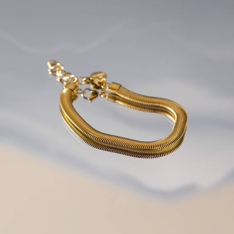 Flow Armband glänzend in 18K Gold mit Schlangenstruktur, elegant inszeniert auf sanftem Wasserreflex, PURELEI.