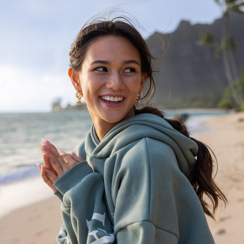 Feminine Ohrringe von PURELEI, goldfarben, am Strand getragen, strahlende Stimmung.