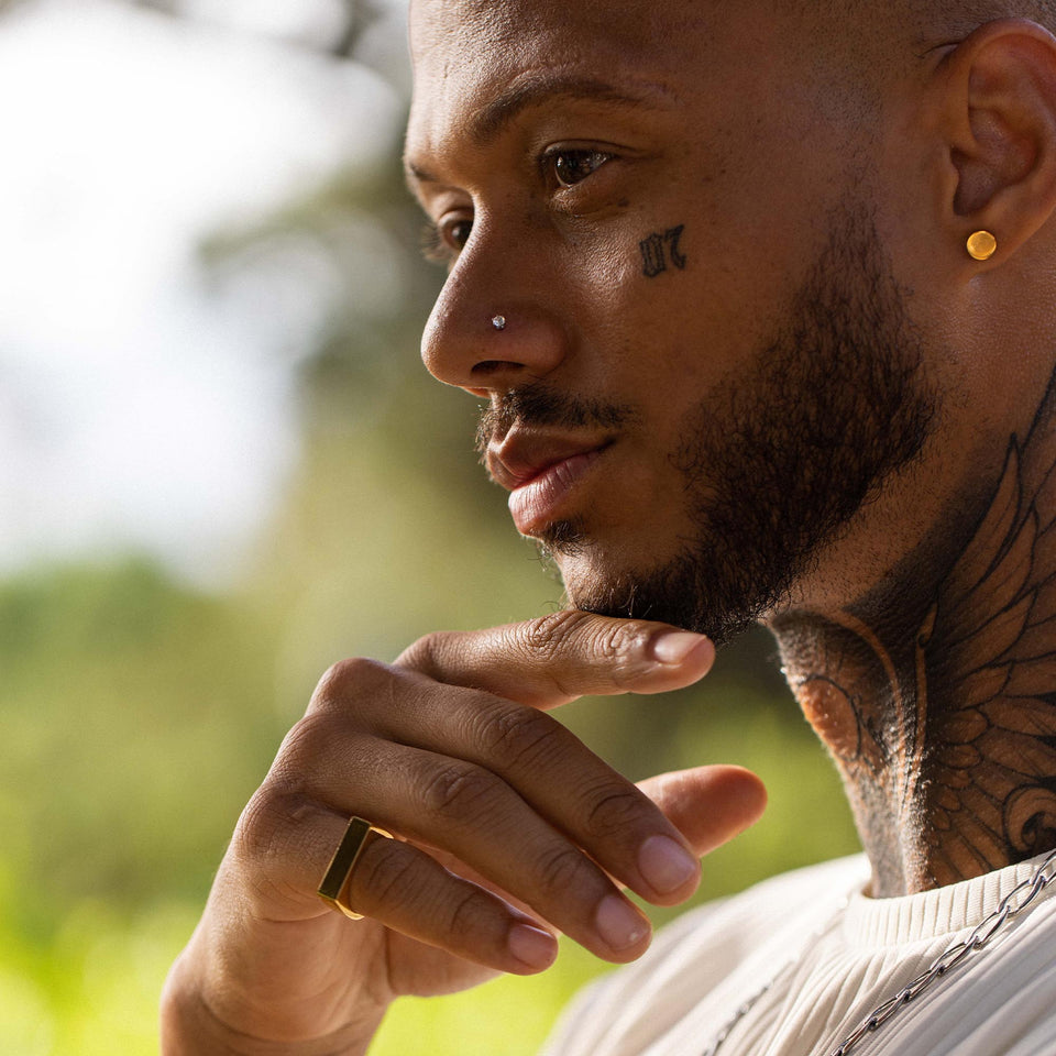 Eleganter Ring aus Gold, getragen von einem Mann mit Tattoos, PURELEI inspiriert.