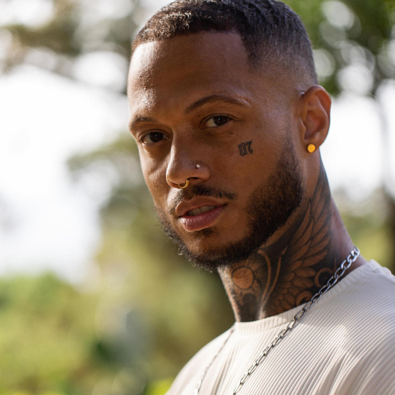 Mann mit Kette und Tattoos, natürliche Umgebung, PURELEI inspiriert.