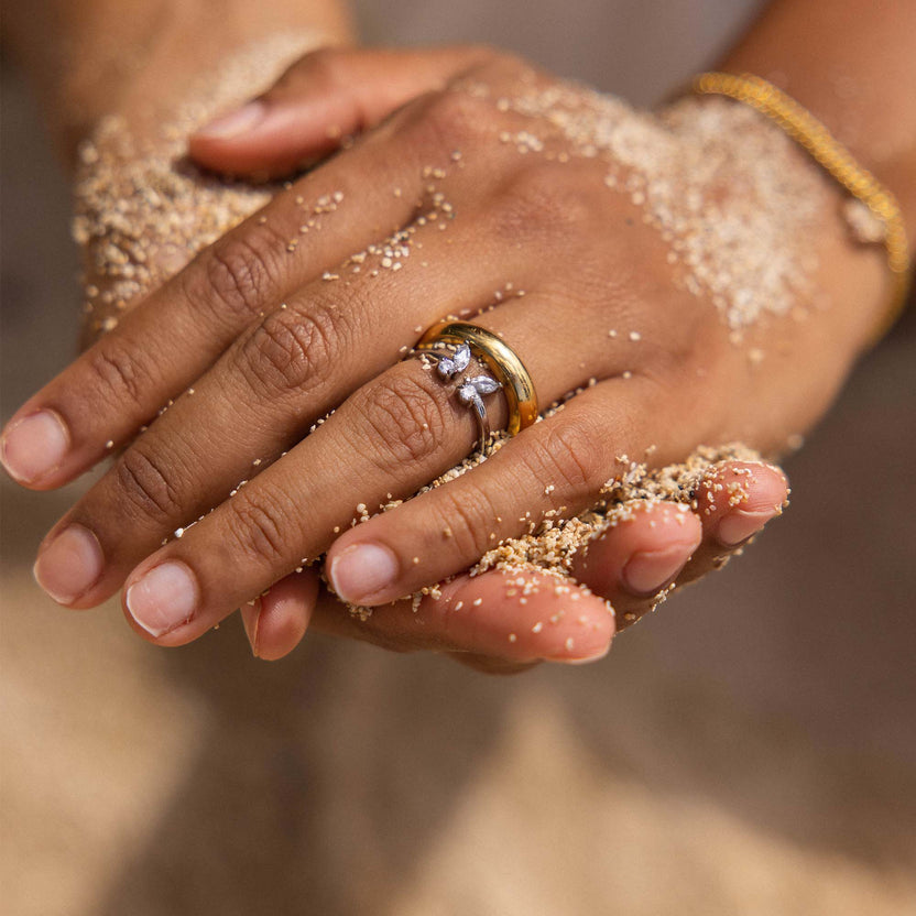 Silberner Ring mit floralem Design, getragen in sandiger Umgebung – PURELEI.